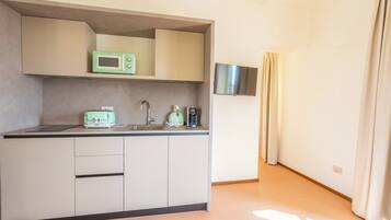 Eine kompakte Küche mit Mikrowelle, Toaster und Wasserkocher, einem kleinen Spülbecken und einem an der Wand befestigten Flachbildfernseher.