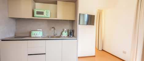 A compact kitchen with a microwave, toaster, and kettle, a small sink, and a flat-screen TV mounted on the wall.