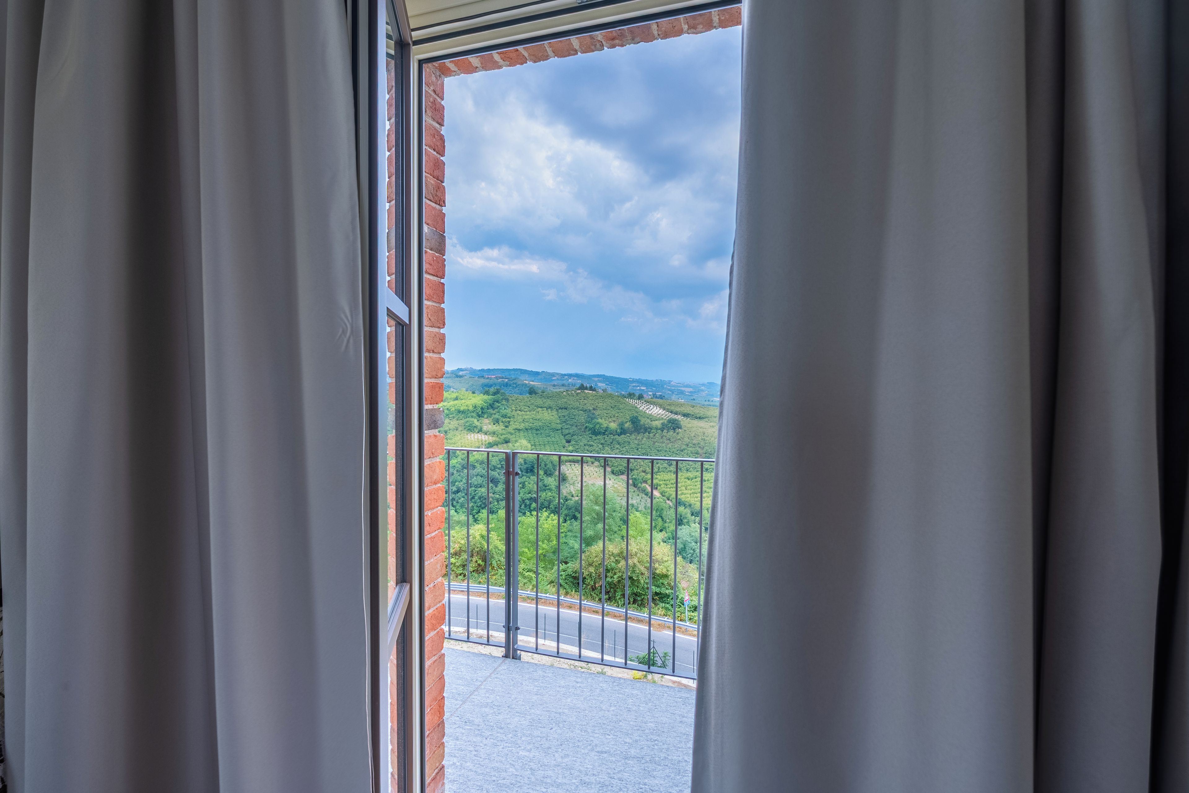 Une vue depuis un balcon doté d’une rambarde en métal, donnant sur un paysage verdoyant et une route.