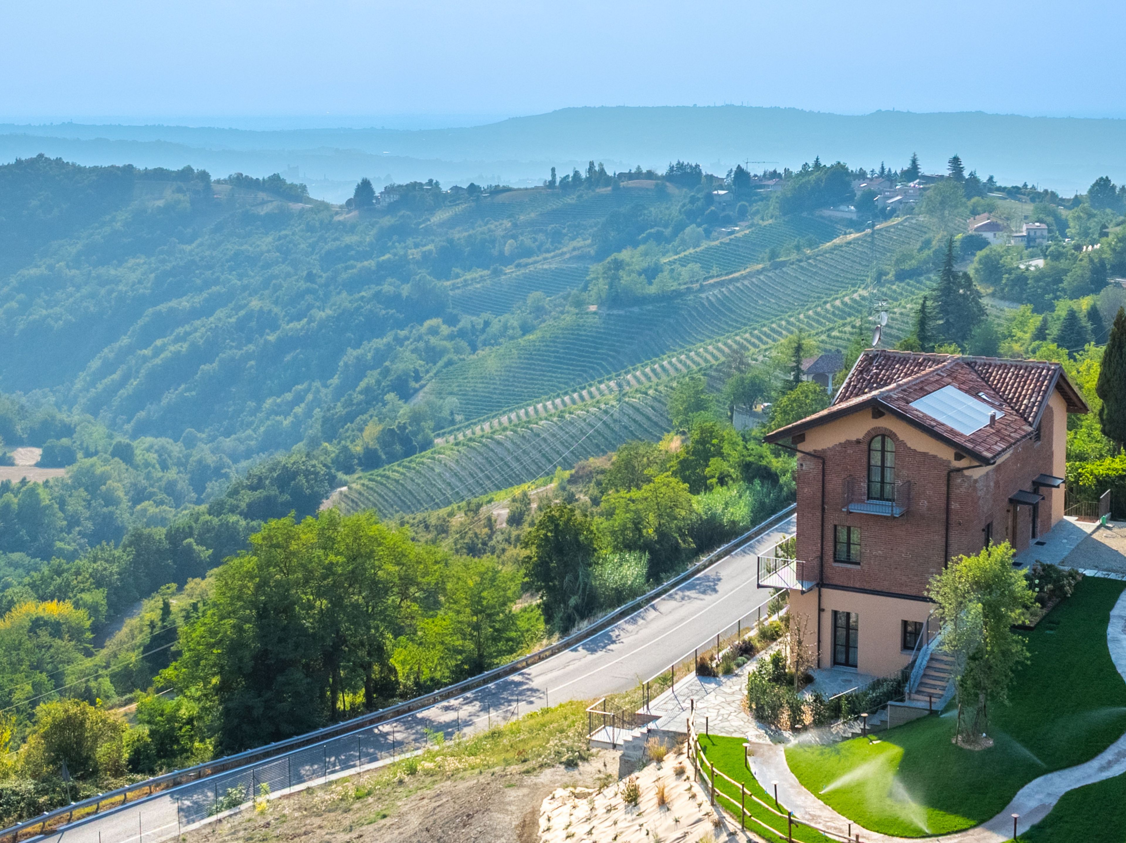 A rural landscape with terraced vineyards, a road, and a building with a sloped roof.