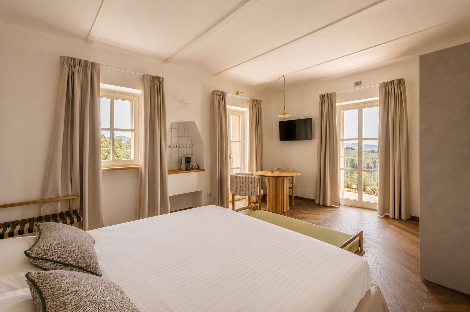 A hotel room with a bed, a desk, a chair, a TV, and large windows.