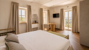 Een hotelkamer met een bed, een bureau, een stoel, een televisie en grote ramen.