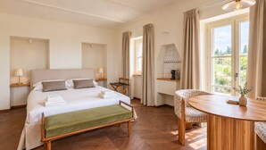 Een hotelkamer met een bed, nachtkastjes, een stoel, een klein tafeltje en uitzicht op het groen.