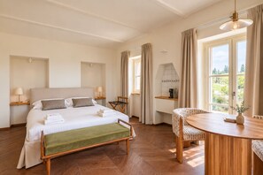 Quarto de hotel com cama, mesas de cabeceira, uma cadeira, uma pequena mesa e vista para o exterior.