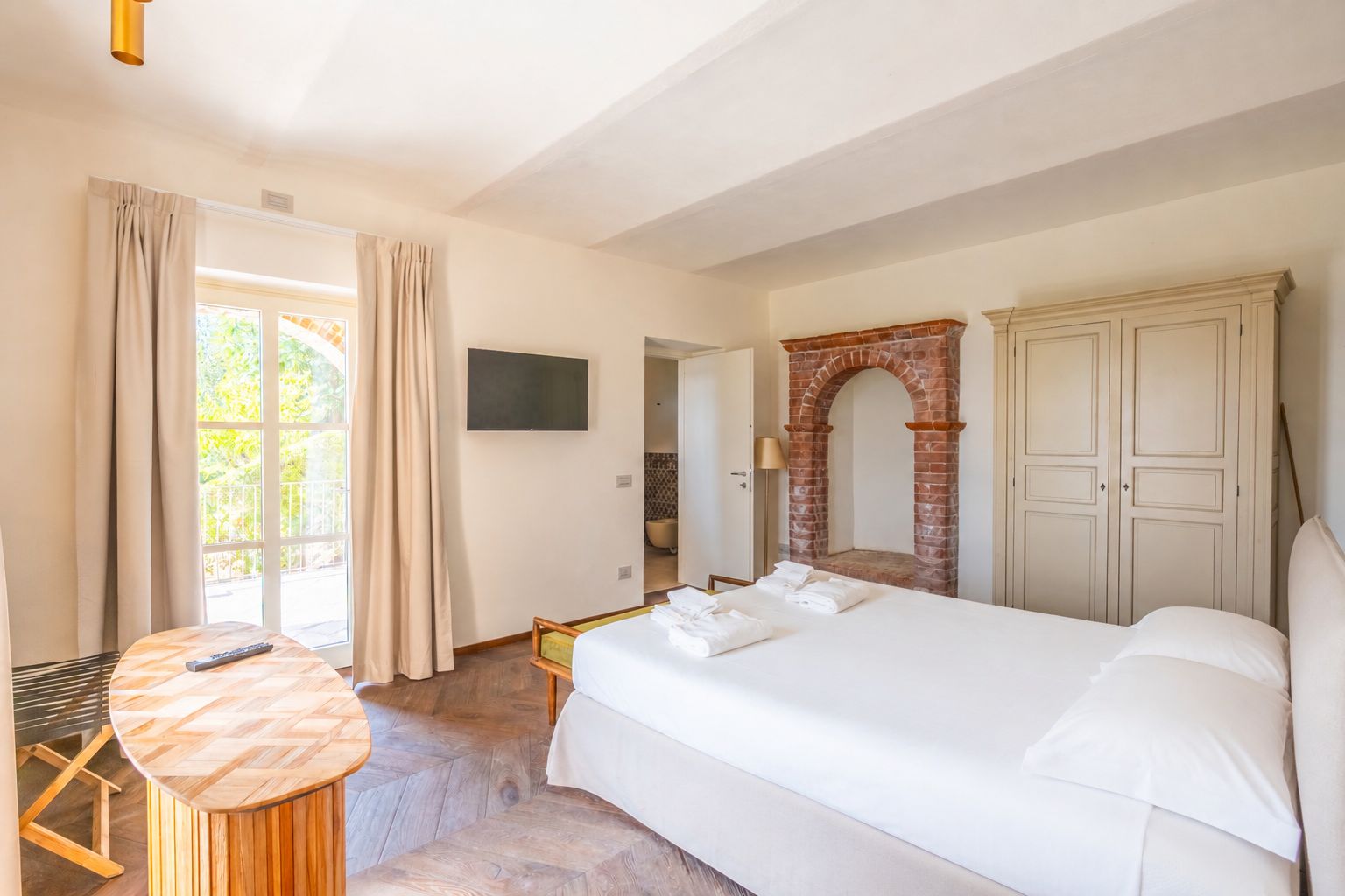 Une chambre d’hôtel avec un lit, une table ronde en bois, un téléviseur, une cheminée en briques et une armoire.