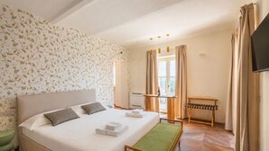 Ein Hotelzimmer mit einem Bett, einer Sitzbank, einem Tisch mit einer Flasche und einem Fernseher.