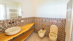 Ein Badezimmer mit einem Holzkosmetikschrank, einem weißen Waschbecken, einer Toilette und einem Spiegel.