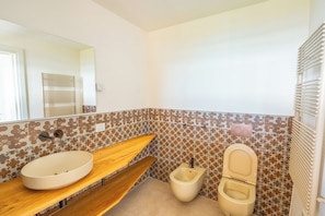 Casa de banho com toucador de madeira, lavatório branco, sanita e espelho.