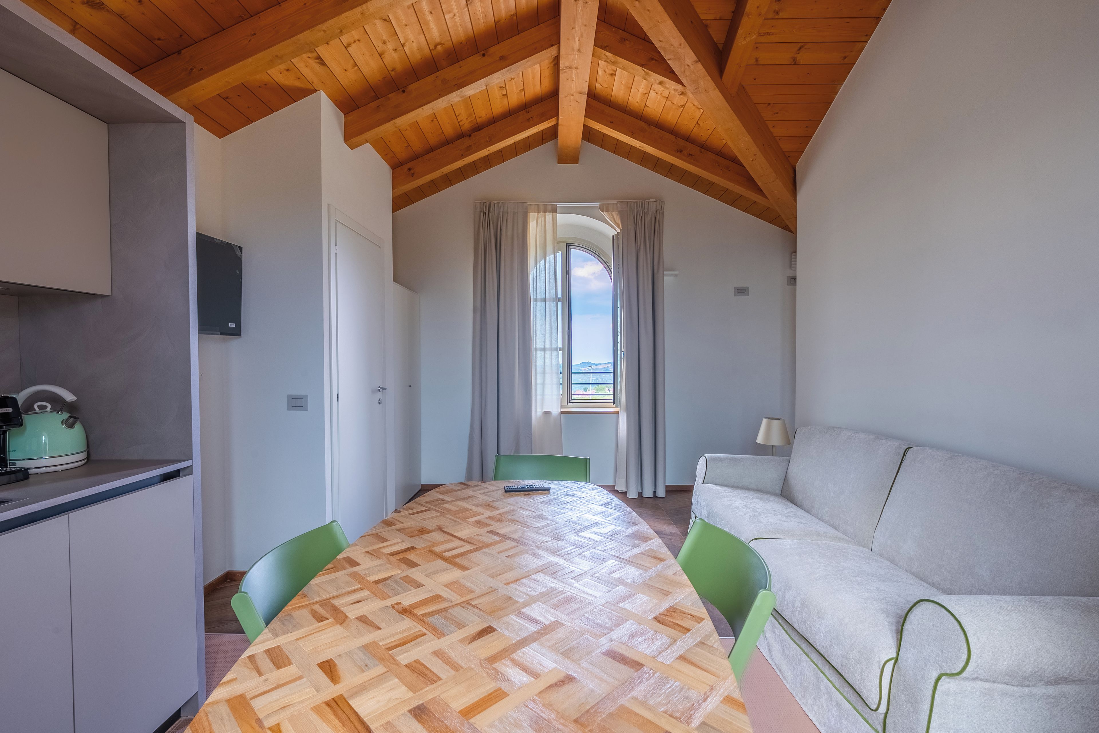 Ein Zimmer mit Holzboden, einem Esstisch, Stühlen, einer Couch und einem Fenster mit Vorhängen.