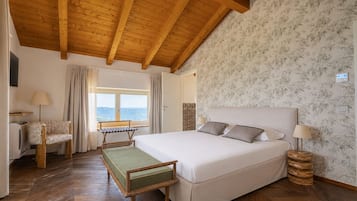 A bedroom with a large bed, wooden beams, a window with a view, a desk with a chair, and a patterned wall.