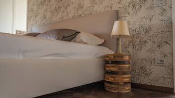 Un letto con un cuscino decorato, una lampada da comodino su un piedistallo in legno e una parete rivestita con carta da parati a motivi di bambù.