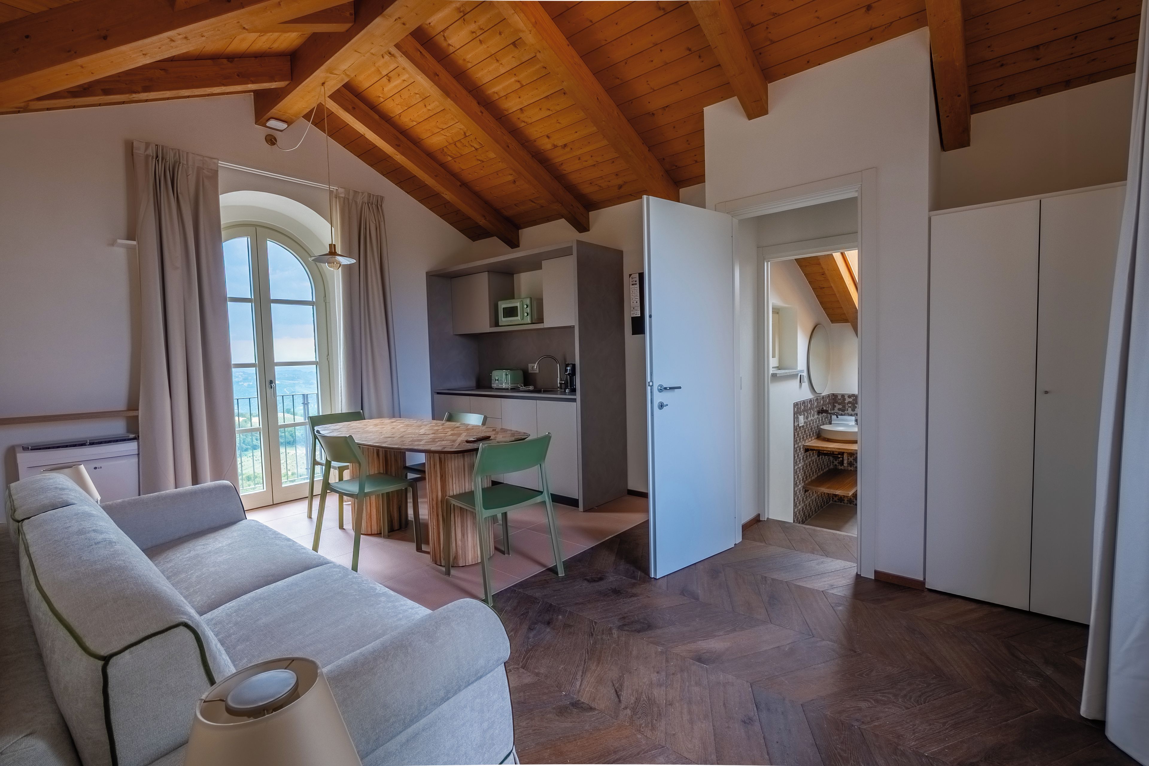 Ein modernes Interieur mit Holzboden, einer Essecke mit Tisch und Stühlen, einer Küchenzeile und einem Badezimmer mit Waschbecken und Spiegel.