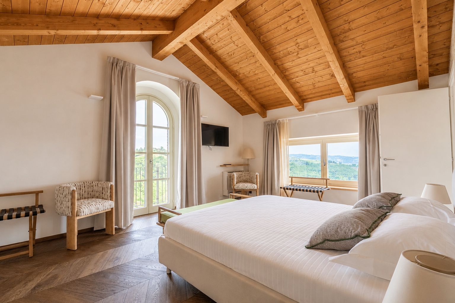 Quarto com cama grande, vigas de madeira no teto, TV, cadeira e janela com vista.
