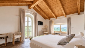 Ein Schlafzimmer mit einem großen Bett, Holzbalken an der Decke, einem Fernseher, einem Sessel und einem Fenster mit Blick.