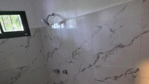 Et badeværelse med toilet, bruser og et lille vindue.