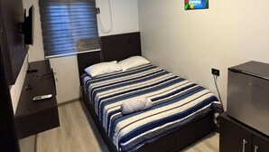 A bedroom with a bed, a window with blinds, an air conditioning unit, a painting on the wall, and a desk with a computer. - Hotel mg (Palenque)