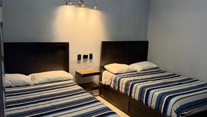 A hotel room with two beds, a ceiling fan, a wall-mounted light fixture, and a small bedside table. - Hotel mg (Palenque)