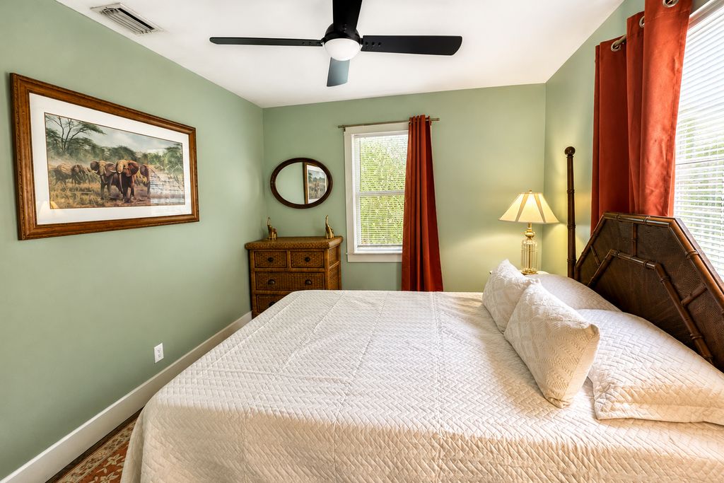 A bedroom with a bed, a ceiling fan, a window with curtains, a dresser, and a framed picture on the wall.