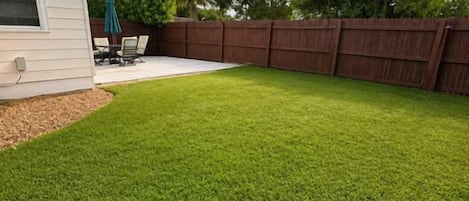 Un patio trasero con cerco de madera, un patio con mobiliario exterior y un césped.