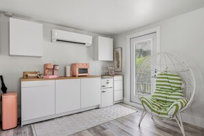 A modern kitchen with white cabinets, a pink coffee machine, and a hanging chair with green stripes. - Palm Beach Pink Studio Farm Stay- Palm Tree & Alpaca / Llama Farm (Palm Beach Gardens)