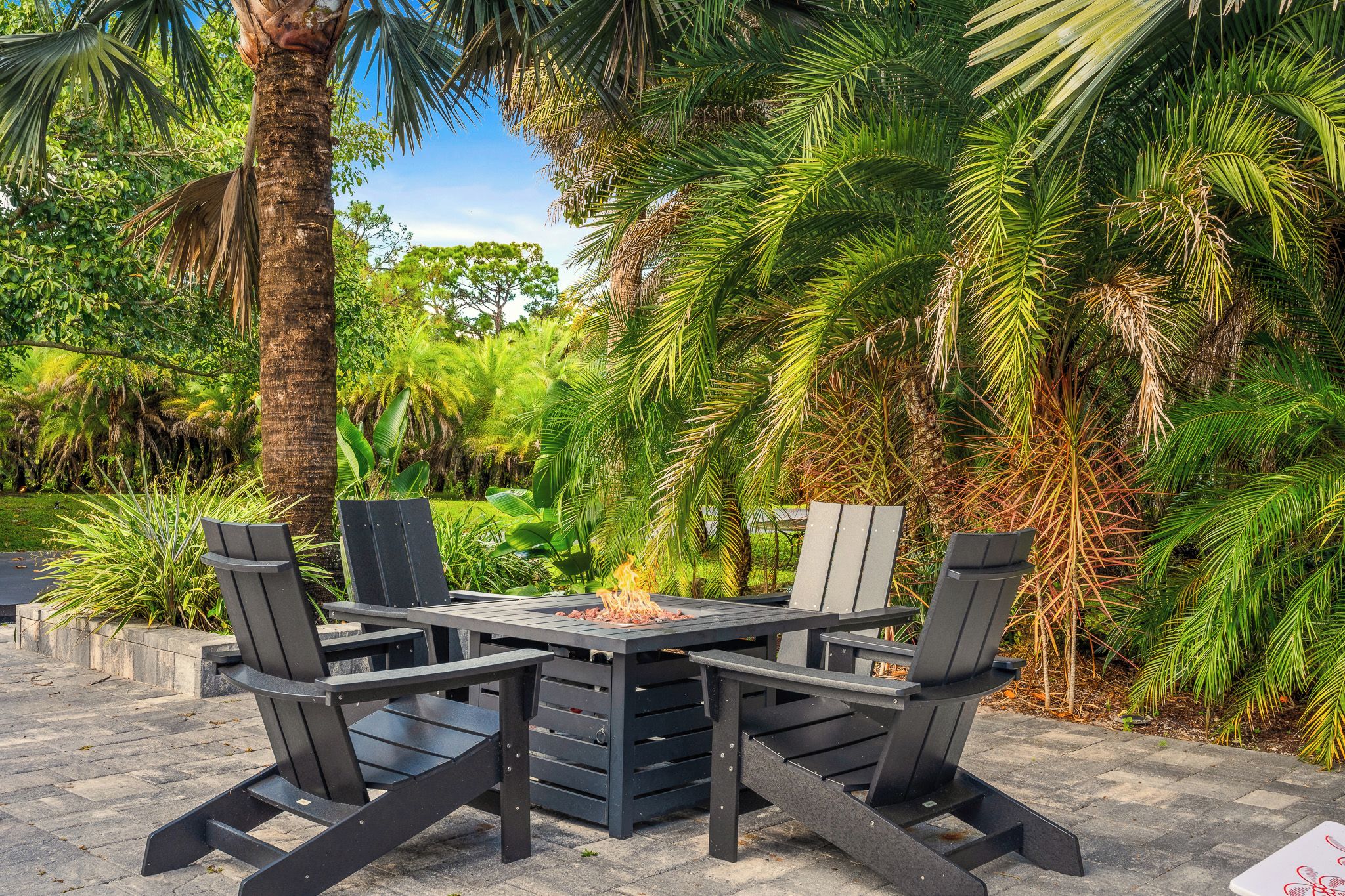 An outdoor seating area with a fire feature, surrounded by lush greenery and palm trees.