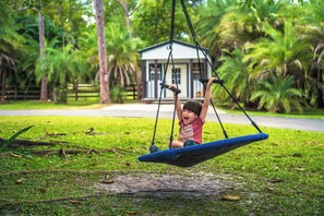 A child on a swing in a grassy area with a building in the background. - Palm Beach Pink Studio Farm Stay- Palm Tree & Alpaca / Llama Farm (Palm Beach Gardens)