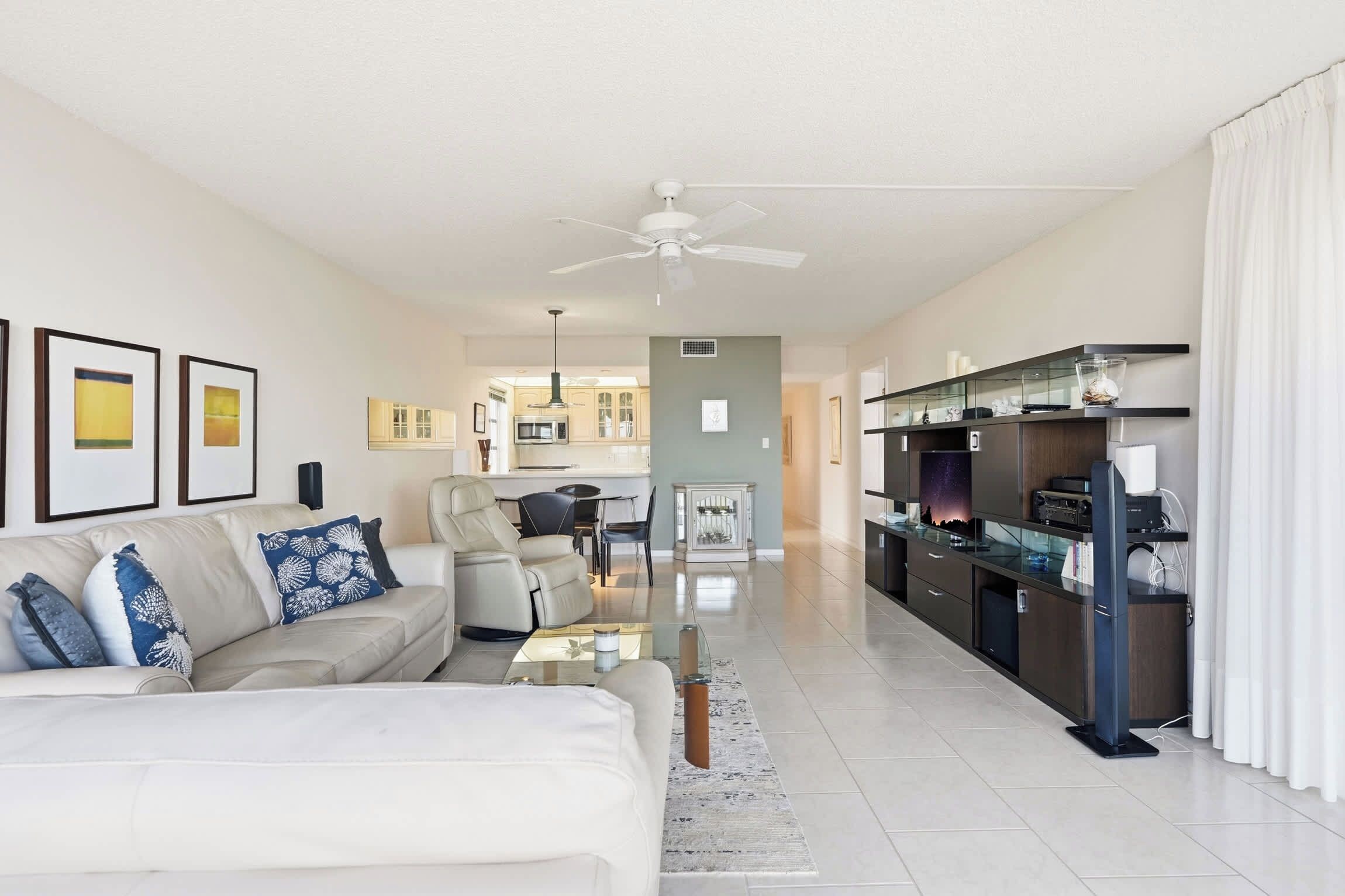 A spacious living room with a white sofa, a dining area, and a kitchen in the background.