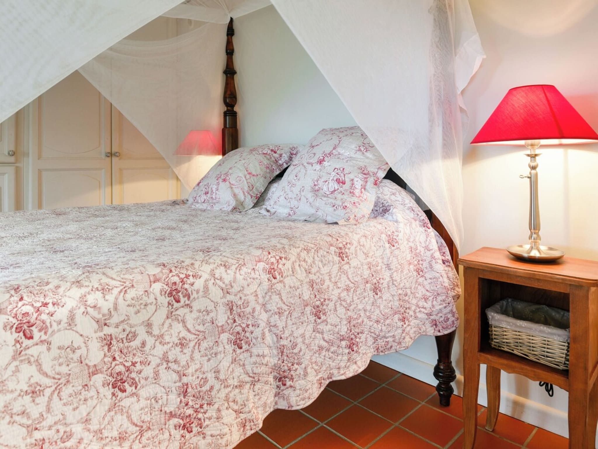 A bedroom with a canopy bed, a bedside lamp, and a nightstand.