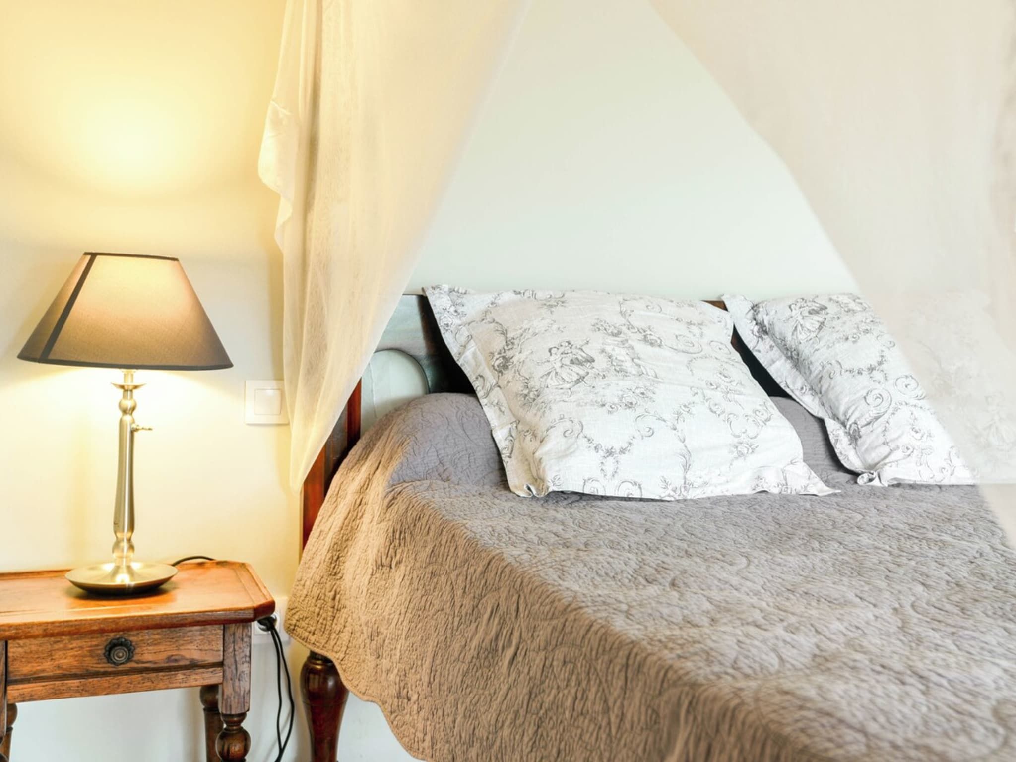 Ein Schlafzimmer mit einem Bett, einer Nachttischlampe und einem Vorhang.