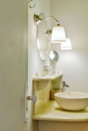 A bathroom with a white sink, a mirror, and a wall-mounted lamp. - Tarrazu – A tropical retreat with a private hot tub and ocean view (Pointe-Noire)