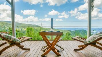 A wooden deck with two lounge chairs, a small table, and a view of a mountainous landscape.