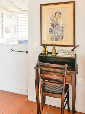 A wooden desk with a framed painting of flowers, a lamp, and a decorative item.