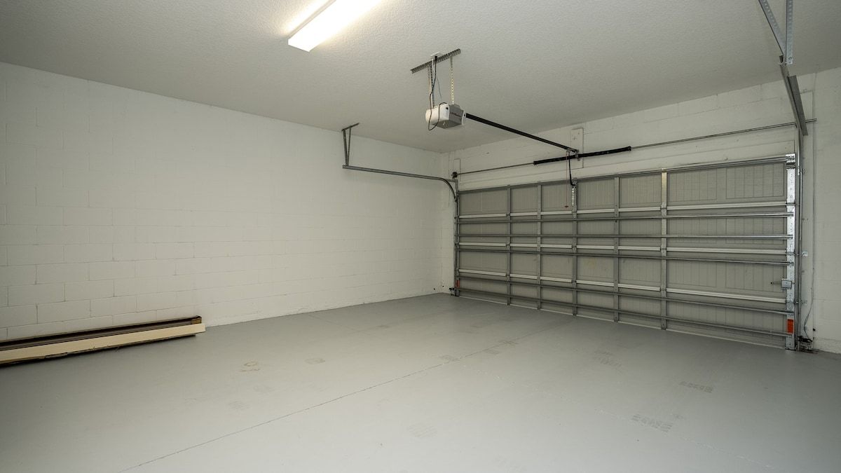 Eine Garage mit geschlossenem Garagentor, einer Deckenleuchte und einem an der Wand befestigten Feuerlöscher.