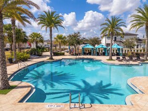 Une piscine dotée d’une terrasse ensoleillée, entourée de palmiers et de chaises longues.