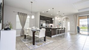 A modern kitchen with a central island, dining area with chairs, and a large window. - Balmoral 4BR Villa Pool & Lake View Near Legoland (Haines City)