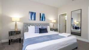 Une chambre d’hôtel avec un grand lit, deux tables de chevet, un miroir et des œuvres d’art abstraites accrochées au mur.