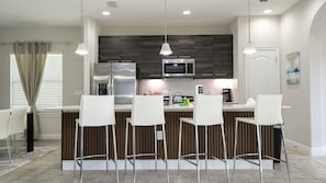 Een moderne keuken met een centraal eiland, barstoelen, roestvrijstalen apparatuur en hanglampen.