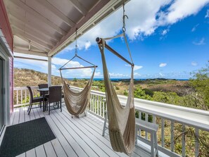 Eine Veranda mit zwei Hängematten, einem Esstisch mit Stühlen und Blick auf die Landschaft.