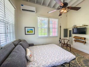 A bedroom with a bed, a sofa, a ceiling fan, a TV, and a window with blinds.