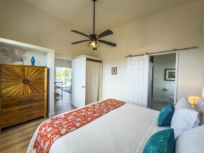 Ein Schlafzimmer mit einem Bett, einem Deckenventilator, einer Holzkommode und einer Tür, die auf einen Balkon führt.