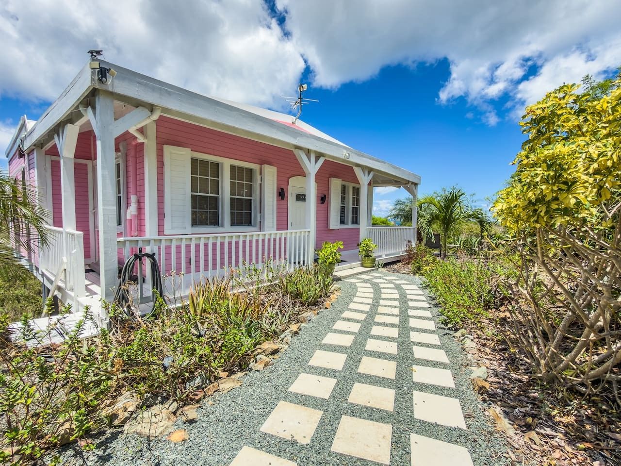 Ein rosafarbenes Haus mit Veranda und einem Kiesweg, der davor führt.