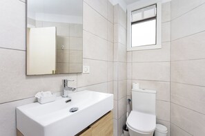 Ein modernes Badezimmer mit einem weißen Waschbecken, einem Spiegel und einer Toilette.