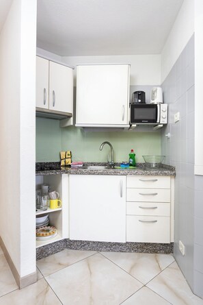 A compact kitchen with white cabinets, a microwave, a sink, and a granite countertop. - Home2Book Sea View Terrace Puerto Santiago (Puerto Santiago)