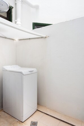 A white washing machine in a corner with a white wall and a window with a green frame. - Home2Book Sea View Terrace Puerto Santiago (Puerto Santiago)