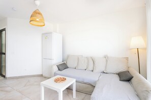 Ein minimalistisches Wohnzimmer mit einer Couch, einem kleinen Tisch, einer Lampe und einer Pendelleuchte.