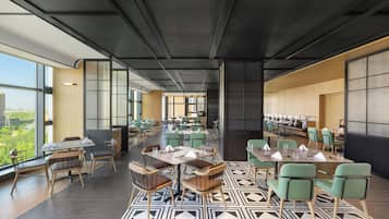 A modern dining area with multiple tables and chairs, large windows offering a view of the city, and a patterned floor.