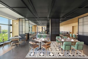 A modern dining area with multiple tables and chairs, large windows offering a view of the city, and a patterned floor.