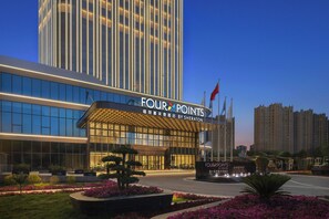 Et hotel med en moderne facade, store vinduer og tydelig skiltning for 'FOUR POINTS BY SHERATON'.