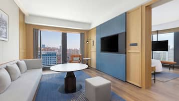 Una habitación de hotel moderna con un ventanal grande, un sofá, una mesa redonda y un televisor.