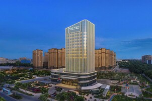 Un hotel moderno con una fachada vertical destacada, una entrada central y un patio ajardinado.